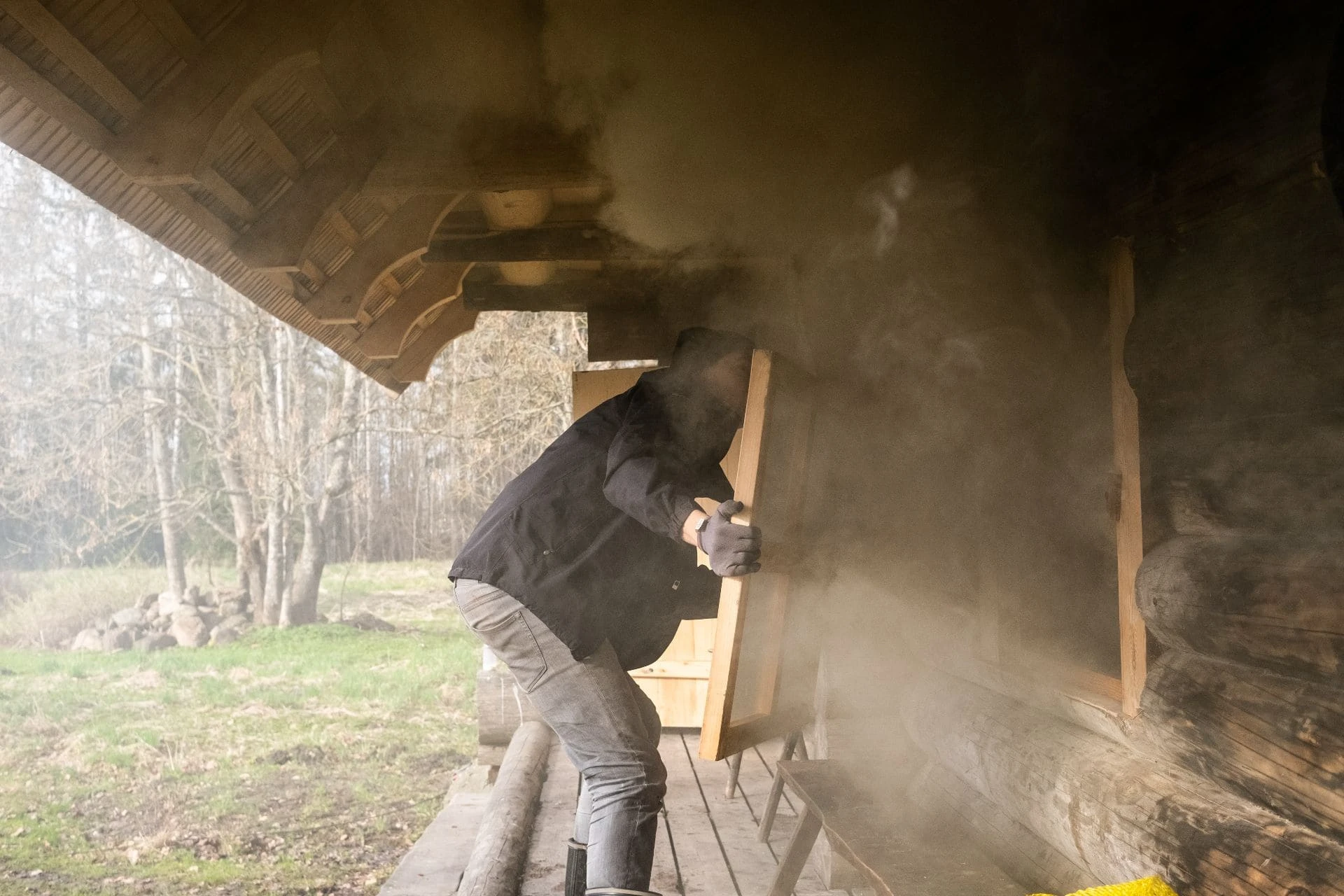 Person opening the window of a traditional Estonian smoke sauna with smoke billowing out