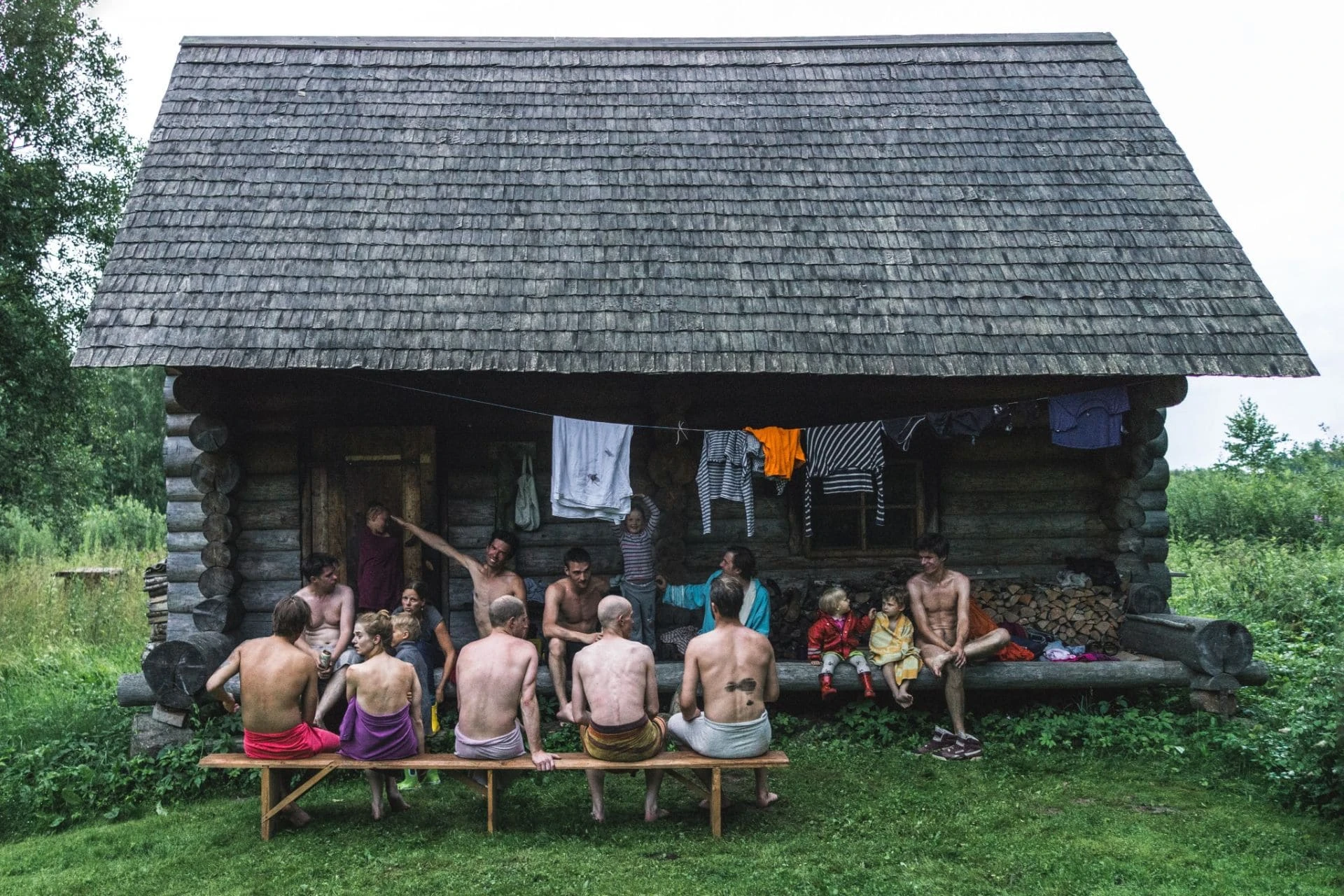 Group of people relaxing in towels outside a traditional Estonian log sauna on a summer day