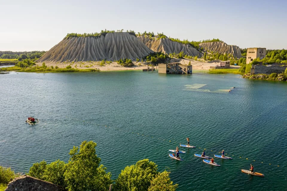 SUP paddlers on the turquoise water of Rummu Quarry with the chalk hill and submerged prison ruins in the background