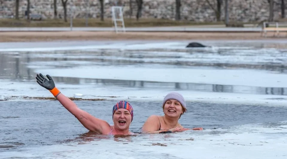 Two women smiling while ice swimming in a frozen Estonian bay in winter