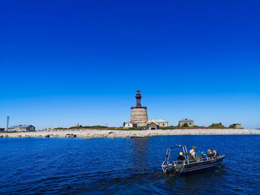 Small boat approaching Keri Island lighthouse with stone beach and blue sky in Estonia