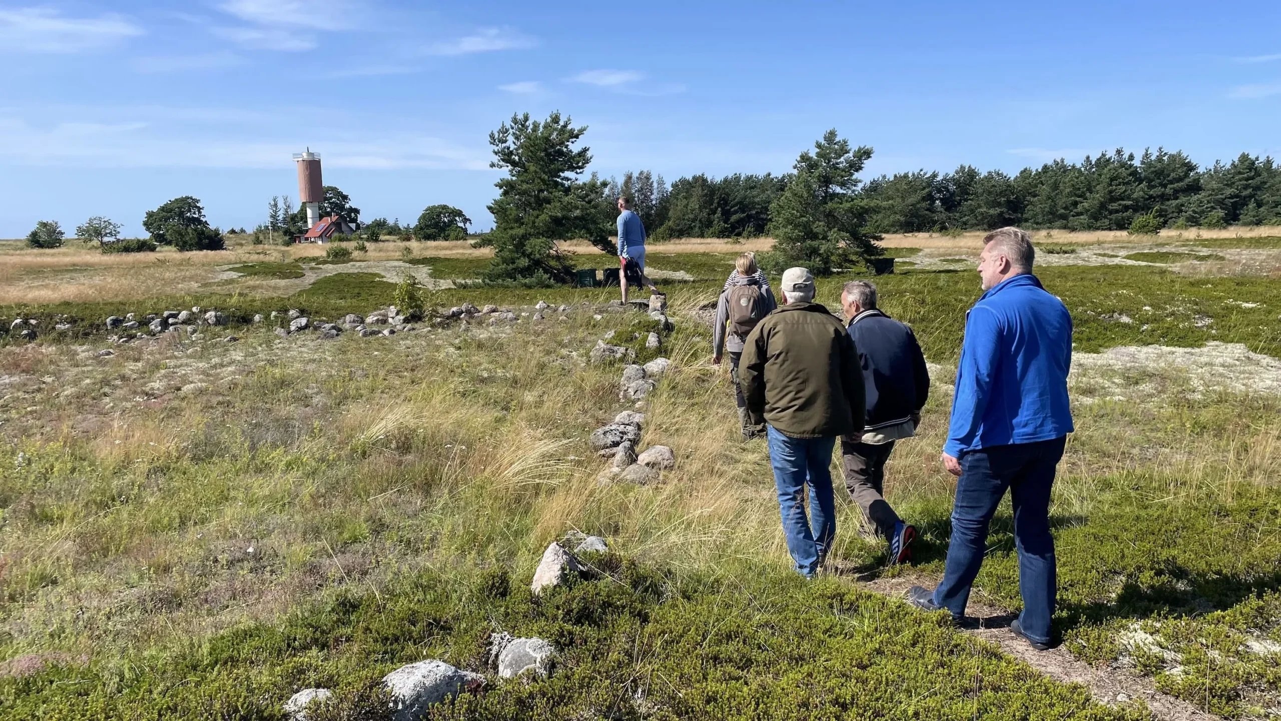 Group of visitors walking across coastal heath toward the lighthouse on Rammu Island in Estonia