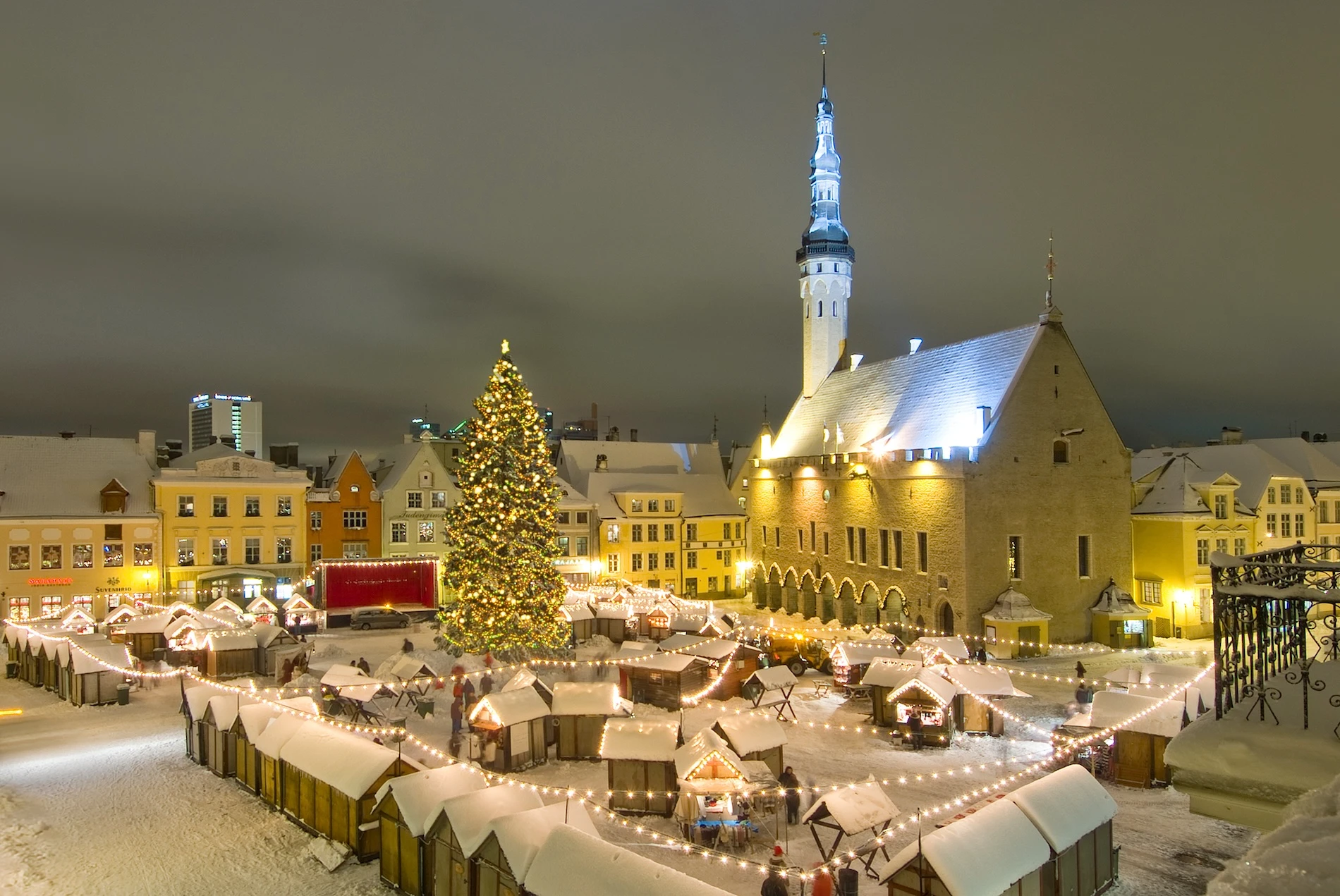 Tallinn Christmas Market on Town Hall Square with a lit Christmas tree, snow-covered wooden stalls and the illuminated Town Hall tower at night