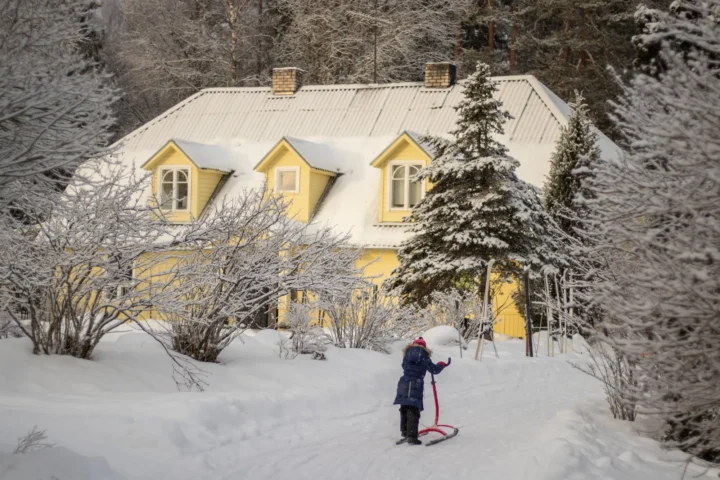Child riding a kicksled near the yellow Uuejärve house in winter Estonia