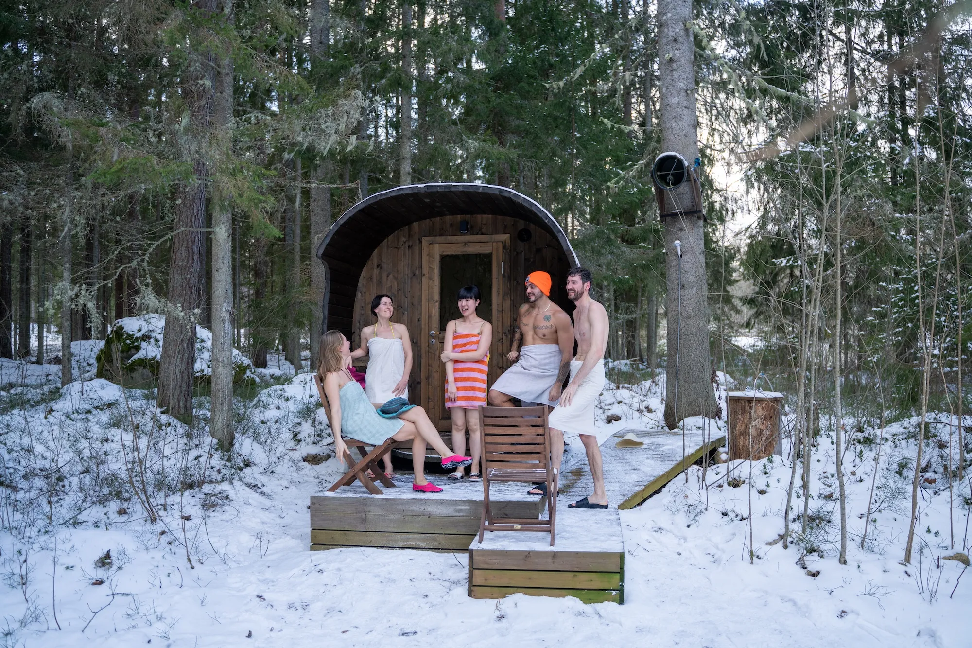 Winter forest sauna experience with a group relaxing outside a wooden barrel sauna in Estonia.