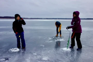 Ice fishing experience on a frozen Estonian lake with participants drilling holes through the ice.