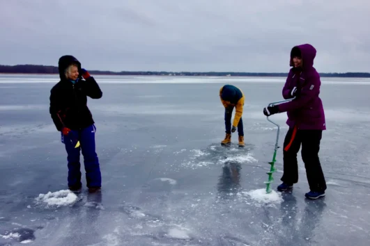 Ice fishing experience on a frozen Estonian lake with participants drilling holes through the ice.