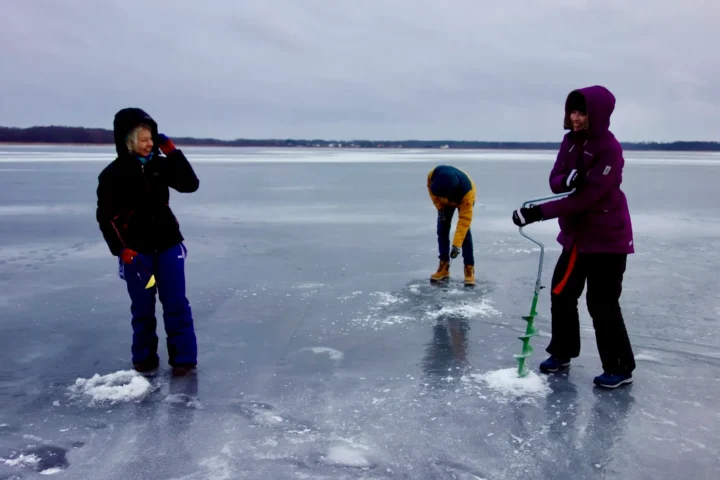 Ice fishing experience on a frozen Estonian lake with participants drilling holes through the ice.