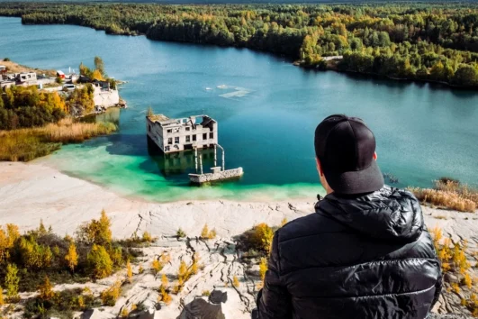 Visitor sitting on Rummu ash hill overlooking submerged quarry Estonia