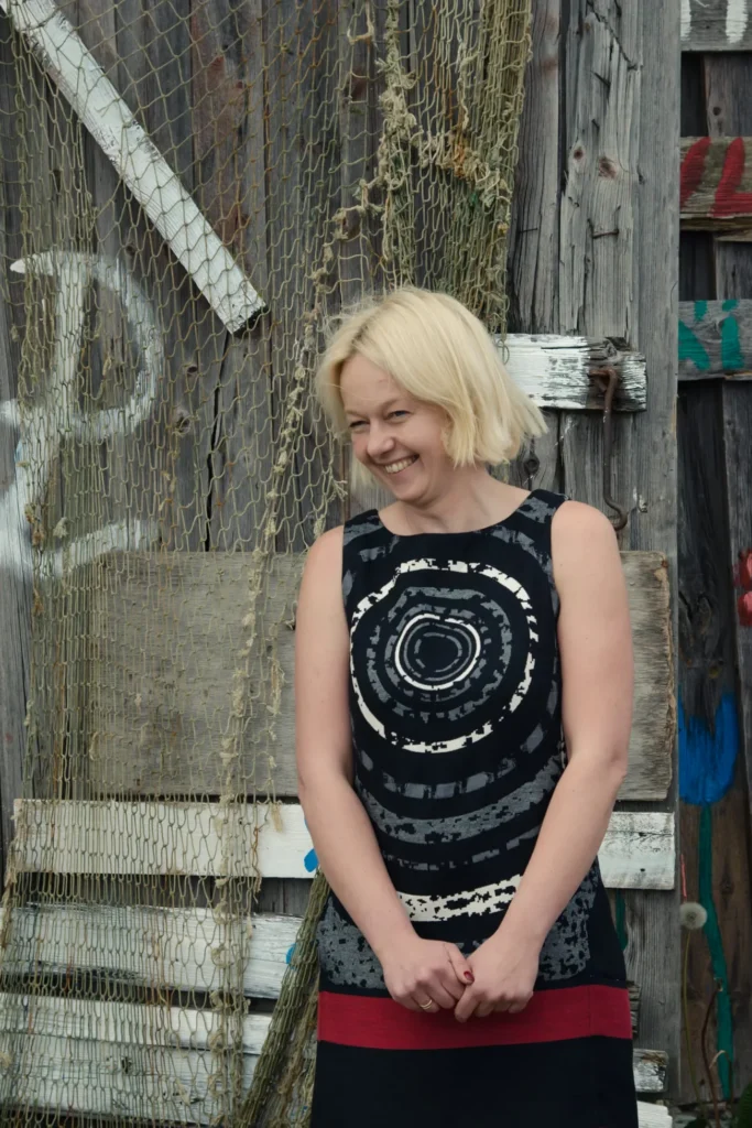 Annika, Founder and CEO of Prangli Travel, smiling in front of a rustic coastal fishing shed in Estonia