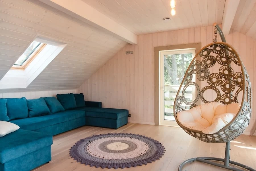 Cosy attic lounge at Villa of Nature Energy on Prangli Island with blue corner sofa and hanging rattan chair