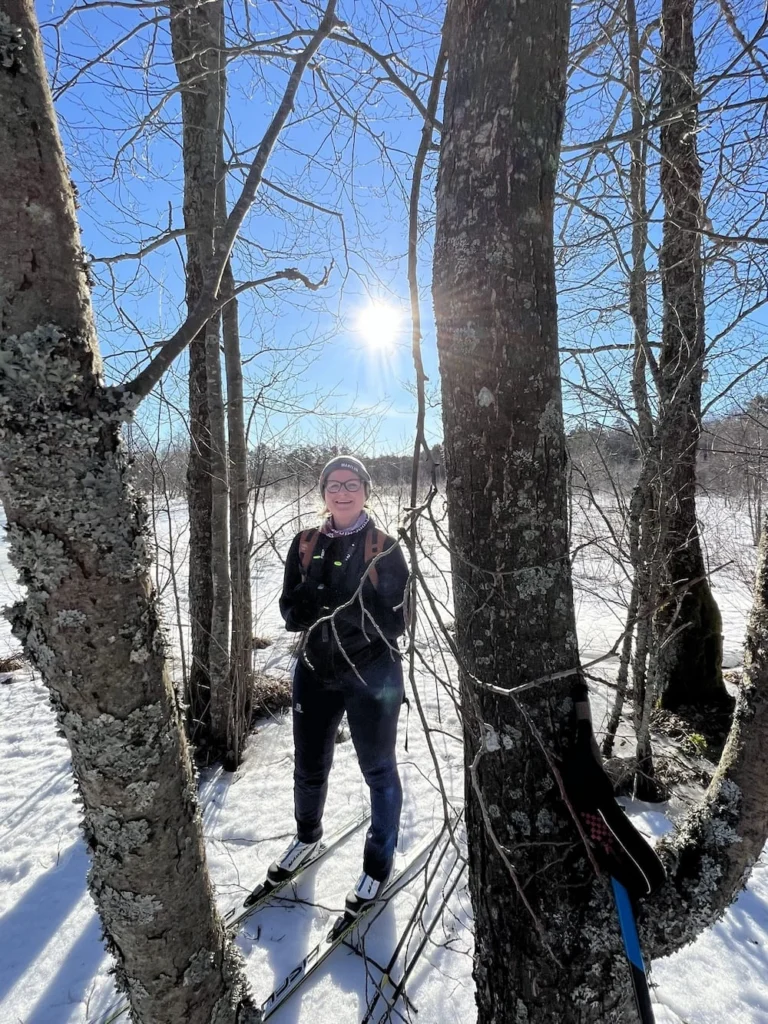 Marilin, tour guide at Prangli Travel, standing on ice skates among snow-covered trees in an Estonian winter forest