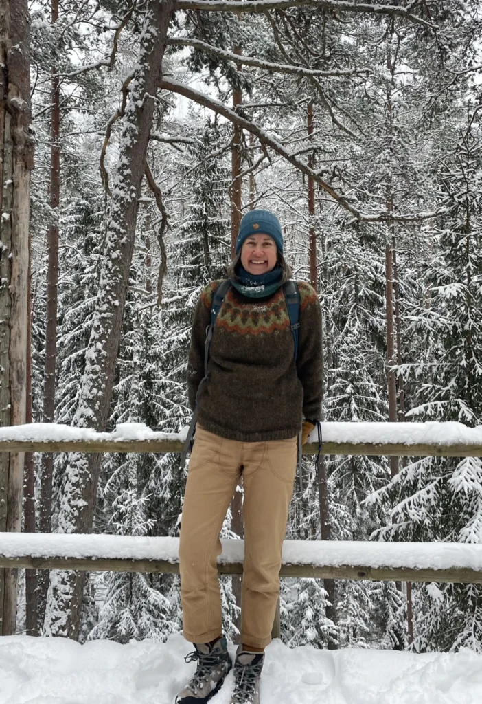 Diana, Tallinn Day Trip guide, standing in a snowy Estonian forest wearing a handknit wool sweater