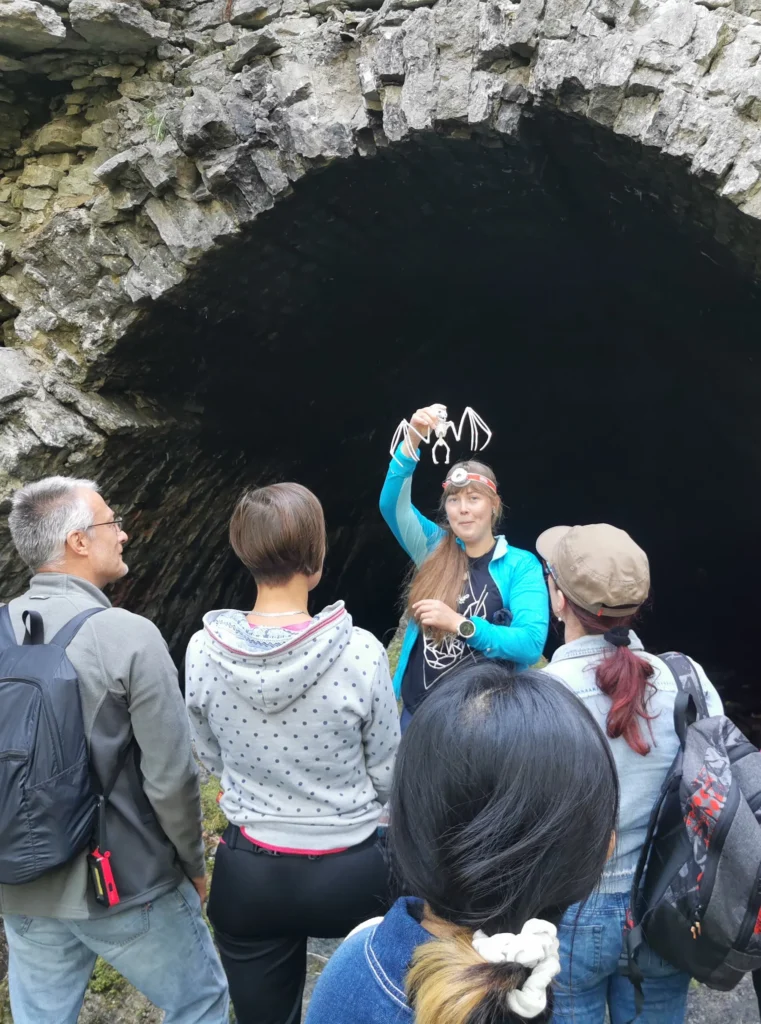 Meriliis, certified hiking guide at Prangli Travel, showing visitors a bat at a cave entrance in Estonia