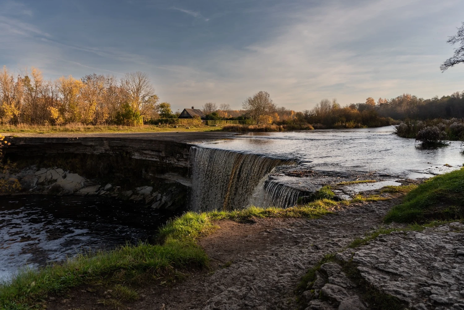 Wide limestone Jägala waterfall flowing over a ledge among autumn trees in Estonia