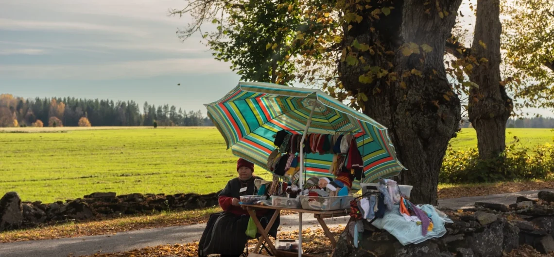 Roadside seller with handmade woollen socks under an umbrella by an autumn field in Estonia