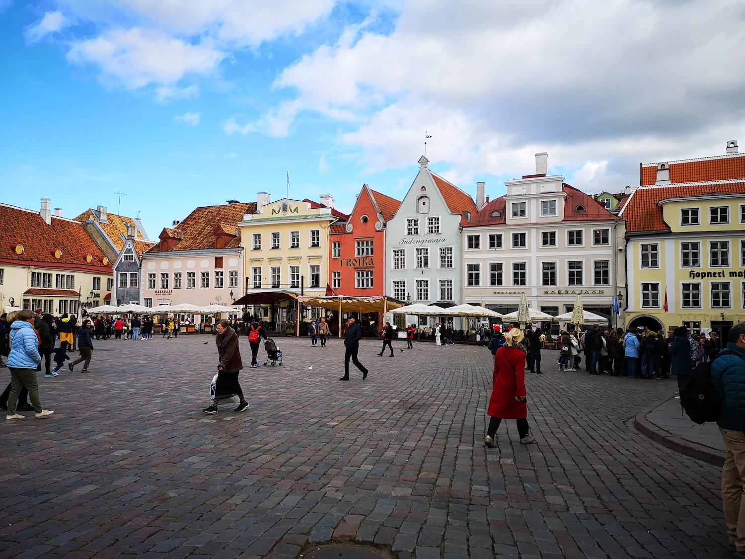 People walking across Tallinn Town Hall Square past colourful merchant houses in autumn